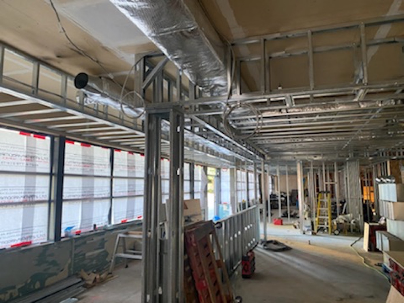 Steel stud walls and ceiling framing beside exterior windows in a commercial interior.